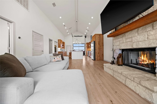 living room featuring light hardwood / wood-style flooring, a fireplace, high vaulted ceiling, and an inviting chandelier