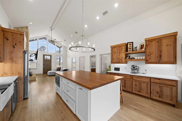 kitchen with stainless steel fridge, ceiling fan with notable chandelier, high vaulted ceiling, white cabinets, and light hardwood / wood-style flooring