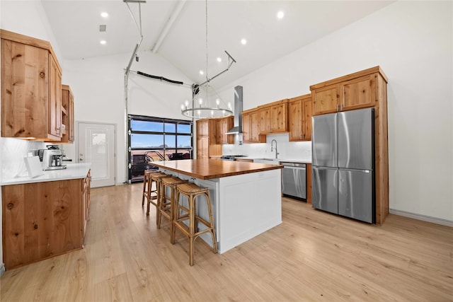 kitchen with stainless steel appliances, high vaulted ceiling, a kitchen island, a notable chandelier, and wall chimney range hood