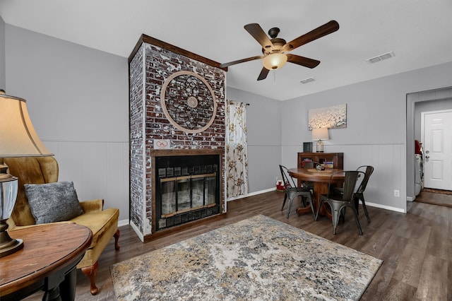 dining room with dark wood-type flooring, a large fireplace, and ceiling fan