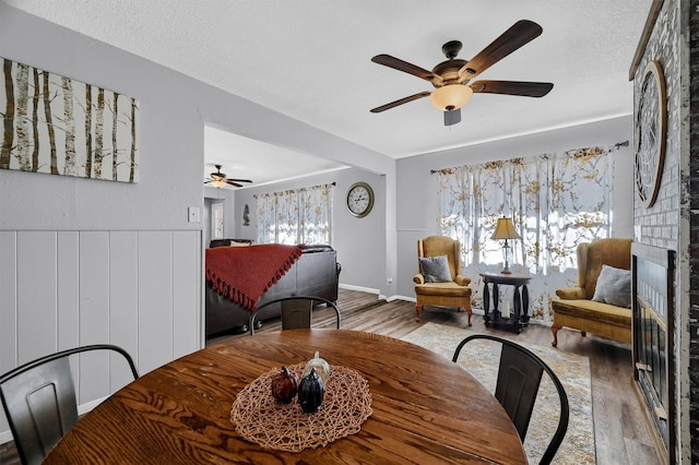 dining room with a brick fireplace, a textured ceiling, wood-type flooring, and ceiling fan