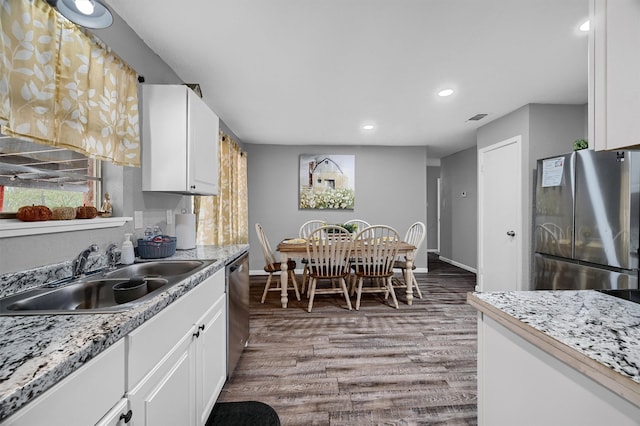 kitchen with white cabinets, appliances with stainless steel finishes, hardwood / wood-style flooring, light stone countertops, and sink