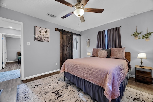 bedroom with ceiling fan, wood-type flooring, and a barn door