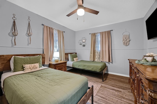 bedroom with vaulted ceiling, ceiling fan, multiple windows, and hardwood / wood-style flooring