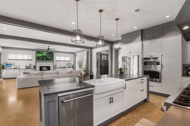 kitchen featuring appliances with stainless steel finishes, decorative light fixtures, sink, white cabinets, and a center island with sink