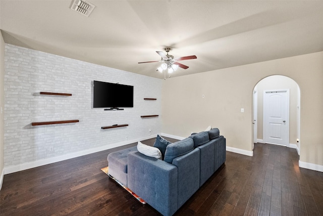 living room with ceiling fan, dark hardwood / wood-style flooring, and brick wall