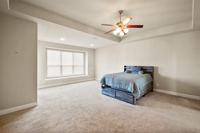 carpeted bedroom with ceiling fan and a tray ceiling