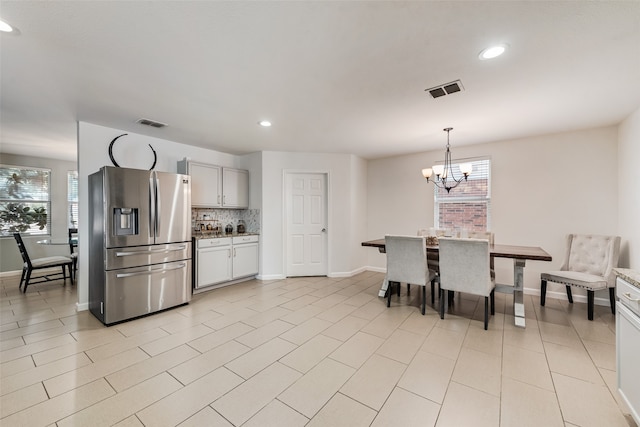 kitchen featuring decorative backsplash, stainless steel refrigerator with ice dispenser, a chandelier, and hanging light fixtures