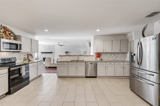 kitchen with tasteful backsplash, sink, a fireplace, white cabinetry, and stainless steel appliances