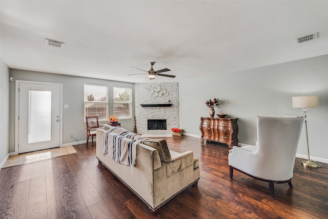 living room featuring a stone fireplace, dark wood-type flooring, and ceiling fan