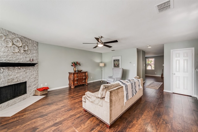 living room with a stone fireplace, dark wood-type flooring, and ceiling fan