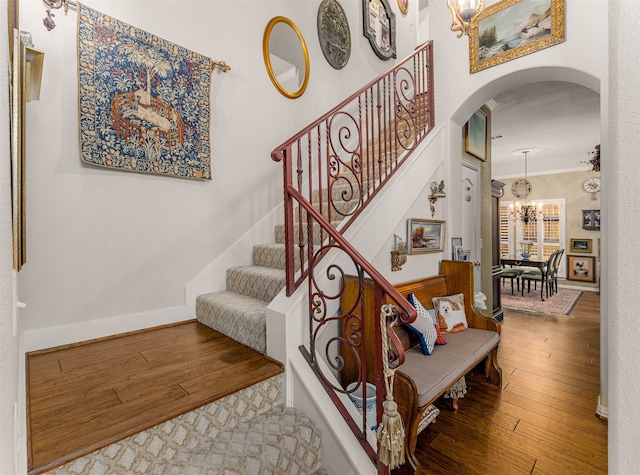 staircase with crown molding, hardwood / wood-style flooring, and a chandelier