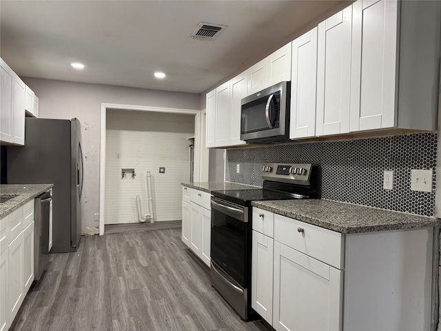 kitchen with tasteful backsplash, appliances with stainless steel finishes, wood-type flooring, white cabinetry, and dark stone countertops