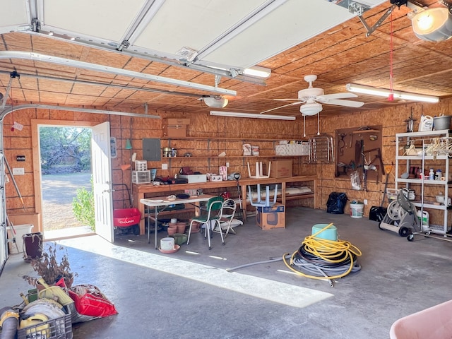 garage with wood walls, a garage door opener, ceiling fan, a workshop area, and electric panel