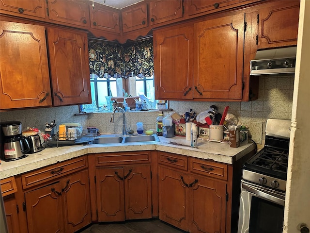 kitchen with light countertops, backsplash, a sink, brown cabinets, and stainless steel gas range oven