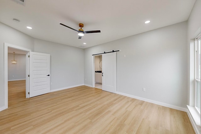 unfurnished bedroom with a barn door, light wood-type flooring, and ceiling fan