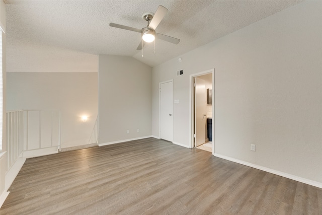 empty room with vaulted ceiling, ceiling fan, a textured ceiling, and light hardwood / wood-style flooring