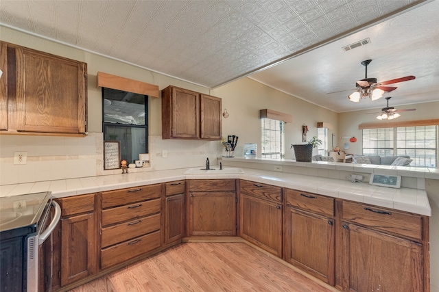 kitchen featuring decorative backsplash, stove, ceiling fan, sink, and light hardwood / wood-style flooring