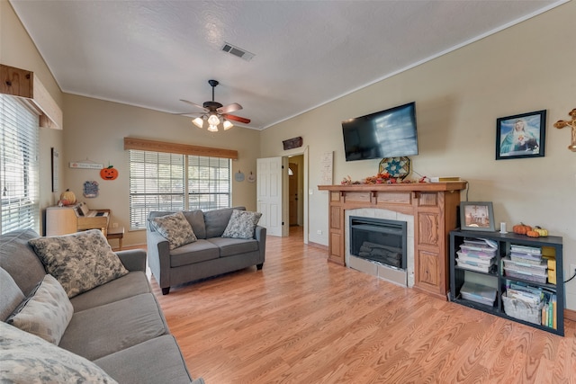 living room with a textured ceiling, ceiling fan, crown molding, light hardwood / wood-style flooring, and a fireplace