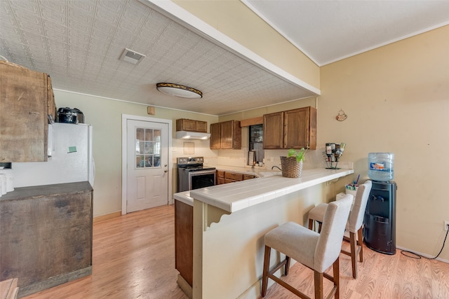 kitchen with electric range, tile counters, a kitchen breakfast bar, light hardwood / wood-style flooring, and kitchen peninsula