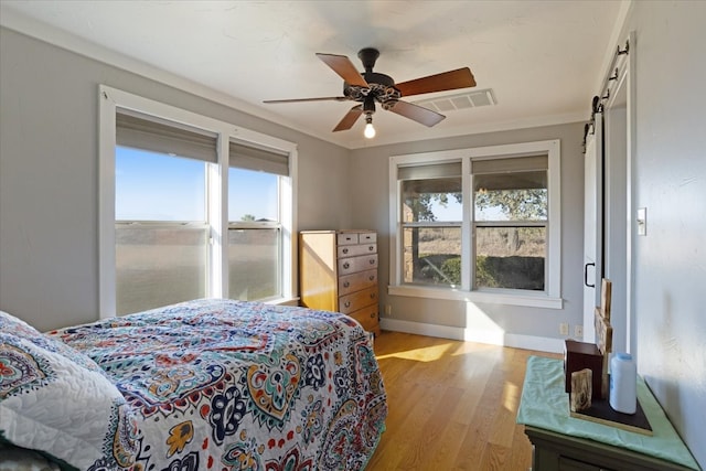 bedroom with ceiling fan, light hardwood / wood-style floors, a barn door, and ornamental molding