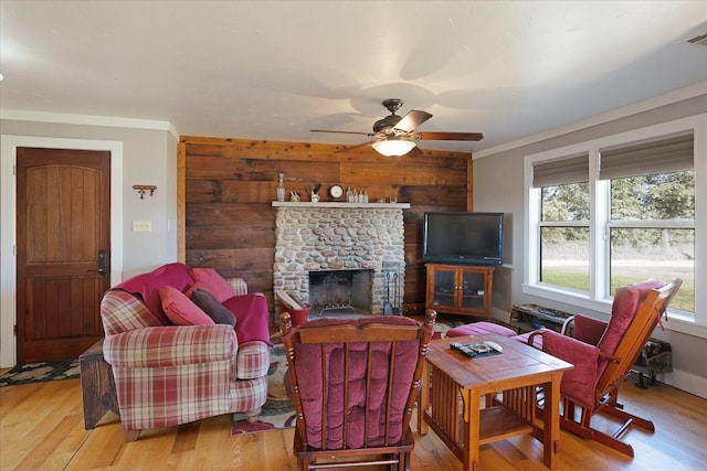 living room featuring hardwood / wood-style floors, a stone fireplace, ceiling fan, and crown molding