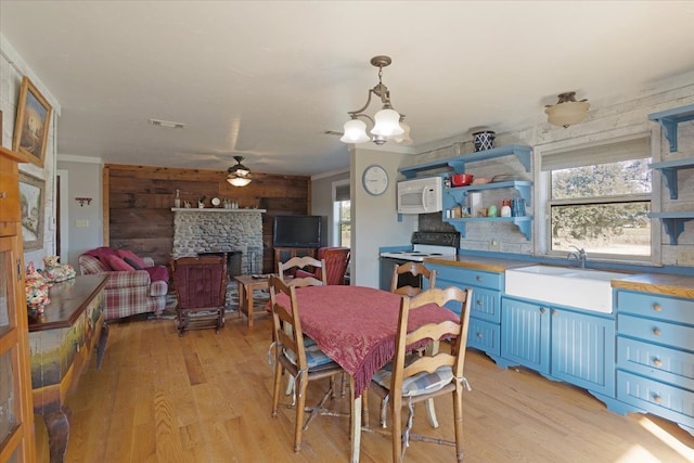 dining room with ceiling fan with notable chandelier, sink, wooden walls, light wood-type flooring, and a fireplace