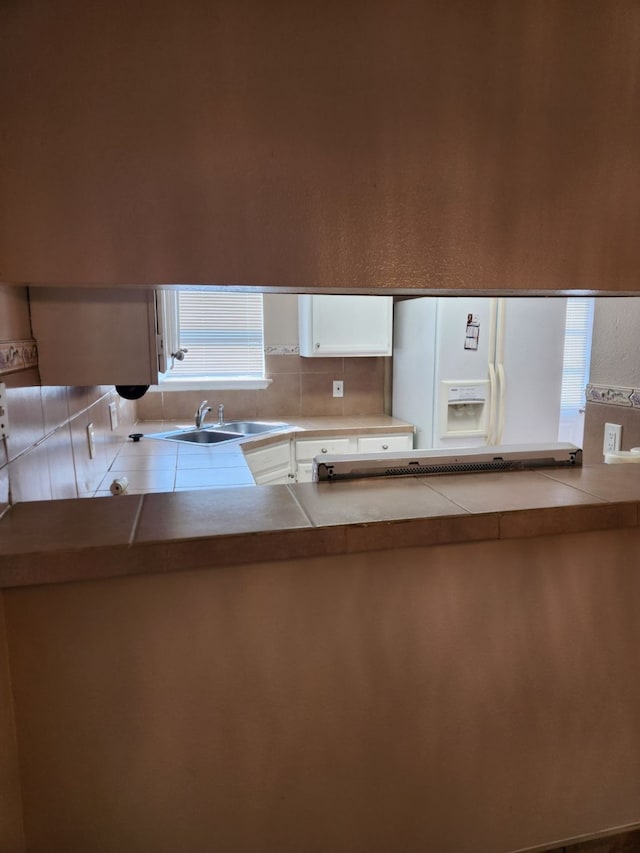 kitchen featuring backsplash, white fridge with ice dispenser, sink, and white cabinets