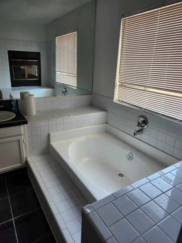 bathroom featuring vanity, a healthy amount of sunlight, tile patterned floors, and tiled tub