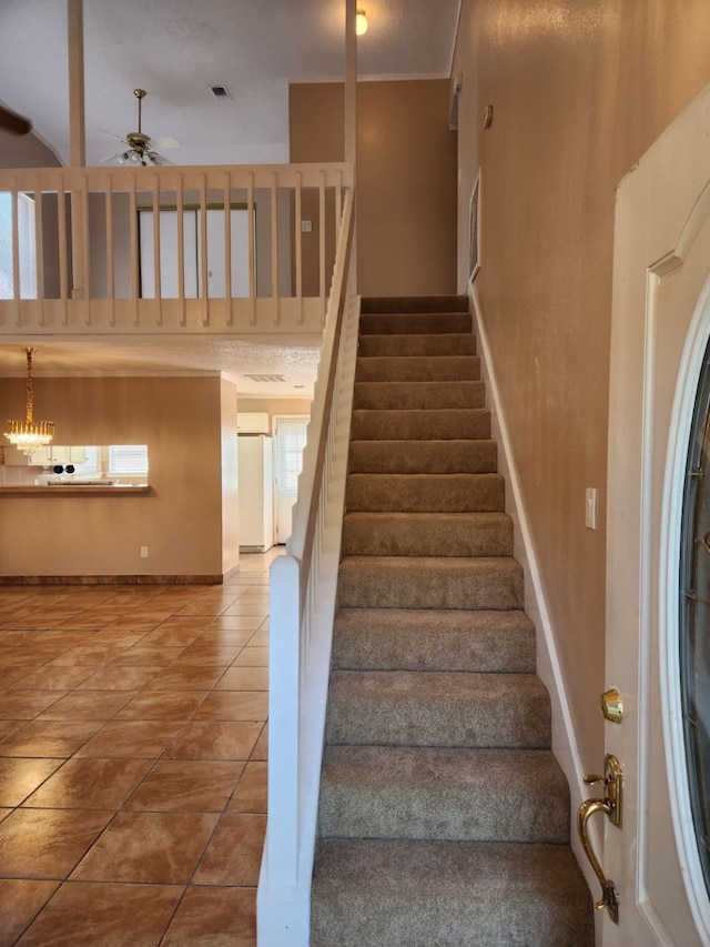 stairway featuring a textured ceiling, ceiling fan with notable chandelier, and tile patterned flooring