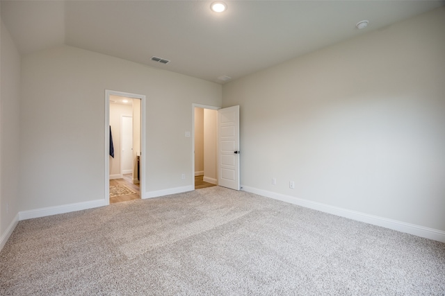 unfurnished bedroom with ensuite bathroom, light carpet, and lofted ceiling