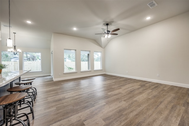 living room featuring a wealth of natural light, vaulted ceiling, dark hardwood / wood-style floors, and ceiling fan with notable chandelier