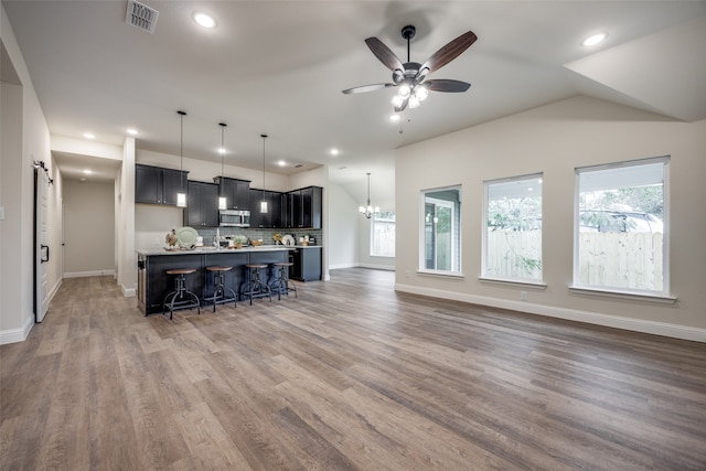 kitchen featuring a kitchen bar, ceiling fan with notable chandelier, hardwood / wood-style floors, decorative light fixtures, and a kitchen island with sink