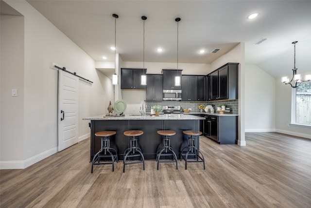 kitchen with a barn door, pendant lighting, light wood-type flooring, appliances with stainless steel finishes, and light stone counters