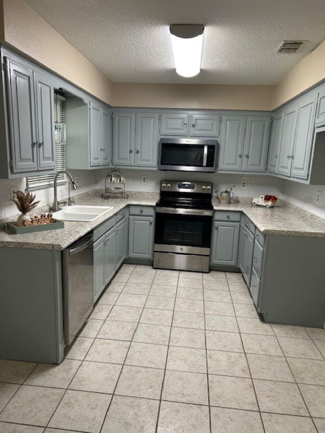 kitchen featuring stainless steel appliances, sink, light tile patterned floors, and gray cabinets