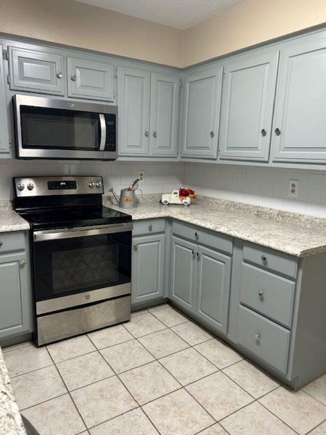 kitchen featuring gray cabinetry, stainless steel appliances, light tile patterned floors, a textured ceiling, and tasteful backsplash