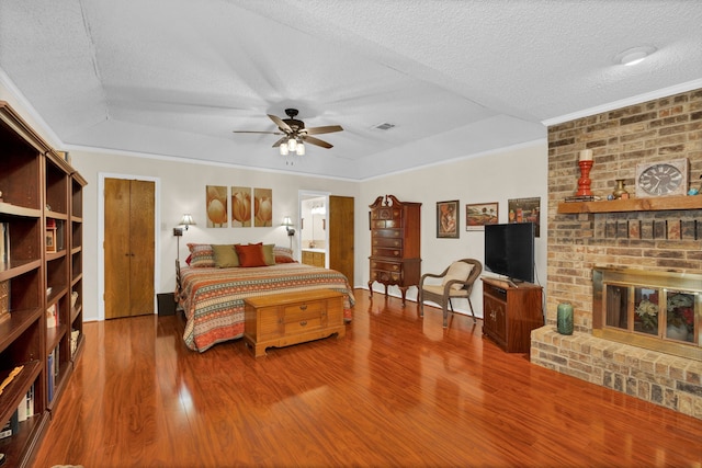 bedroom with ceiling fan, hardwood / wood-style flooring, a textured ceiling, and a brick fireplace