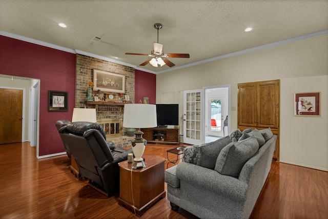 living room featuring dark wood-type flooring, ornamental molding, a brick fireplace, a textured ceiling, and ceiling fan