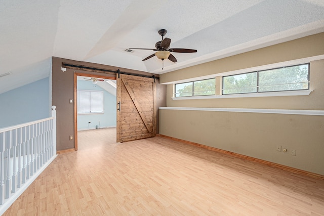 bonus room with a healthy amount of sunlight, vaulted ceiling, a barn door, light wood-type flooring, and ceiling fan