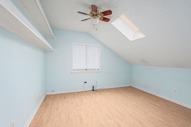 bonus room featuring lofted ceiling with skylight, a textured ceiling, light wood-type flooring, and ceiling fan