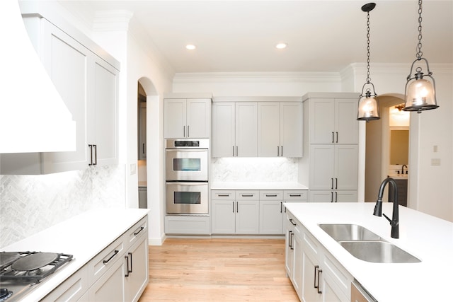 kitchen featuring backsplash, hanging light fixtures, sink, light wood-type flooring, and appliances with stainless steel finishes