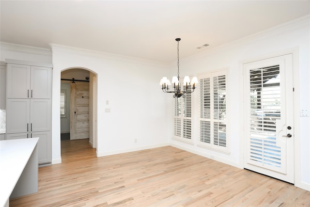 unfurnished dining area with a barn door, light hardwood / wood-style flooring, an inviting chandelier, and ornamental molding