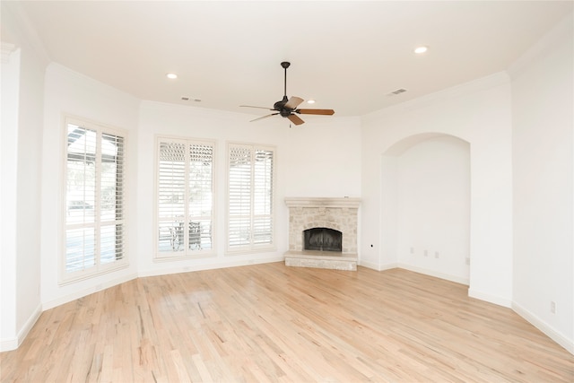 unfurnished living room with light hardwood / wood-style floors, a stone fireplace, ceiling fan, and ornamental molding