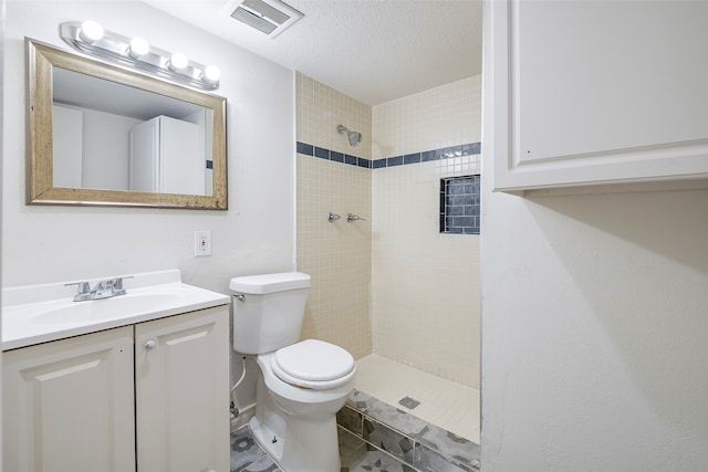 bathroom with vanity, toilet, a textured ceiling, and a tile shower