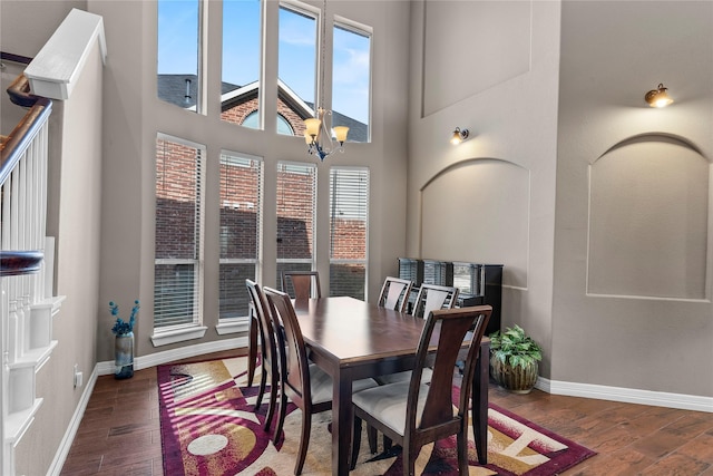 dining space featuring dark wood-type flooring, a towering ceiling, and a notable chandelier