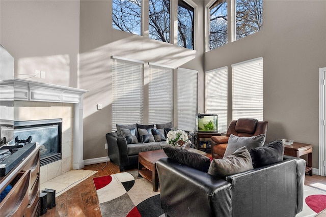 living room featuring light hardwood / wood-style floors, a towering ceiling, and a tiled fireplace