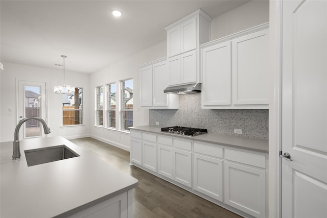 kitchen with tasteful backsplash, under cabinet range hood, light countertops, stainless steel gas stovetop, and a sink