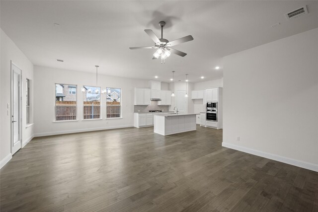 unfurnished living room featuring visible vents, ceiling fan with notable chandelier, dark wood-style floors, recessed lighting, and baseboards