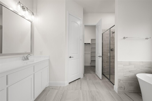 full bathroom with a spacious closet, a shower stall, vanity, and a freestanding tub