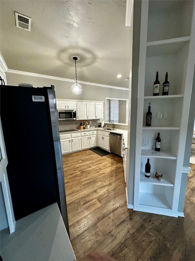 kitchen with dark wood-type flooring, crown molding, white cabinets, pendant lighting, and appliances with stainless steel finishes